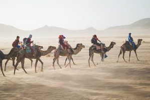 People on camels riding across desert sand storm starting